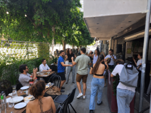 אנשים רוקדים ומתחברים בשמחה לצלילי בוזוקי בקבלת שבת בתחנת אלנבי 104