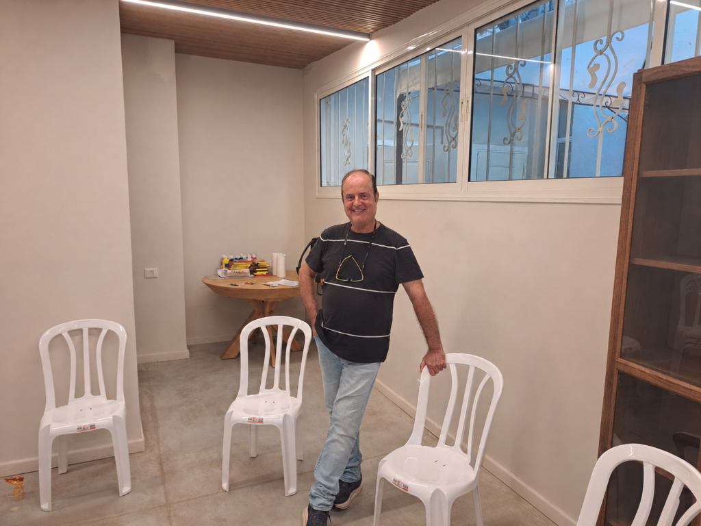 חנן חיים עומד בחלל סדנה עם כיסאות מסודרים לקראת מפגש לנשות מילואימניקים המתמודדות עם השפעות PTSD על התא המשפחתי